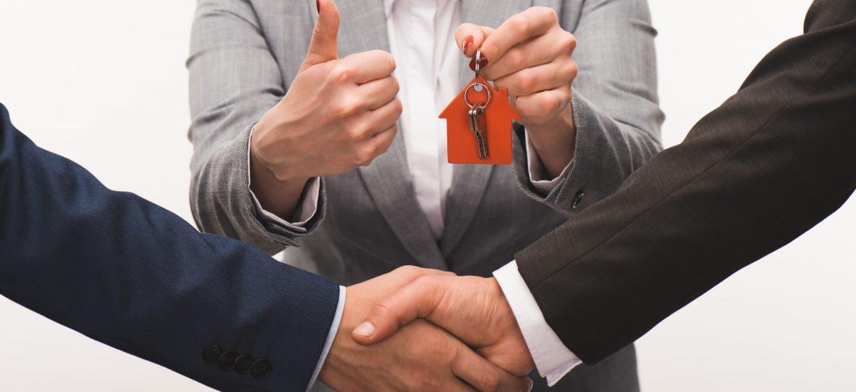 Property for sale by Auction Three people in business attire are depicted. The central person holds a small red house keychain and gives a thumbs up, while the two individuals on either side are shaking hands. A contract and calculator are on the table in the foreground. Presented by World of Auctions