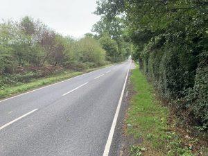 Property for sale by Auction A straight, empty road stretches into the distance, flanked by dense, green trees and bushes on both sides. Located near Plot 10 on Stane Street in Ockley, the smooth, freshly paved surface features crisp white lane markings. The surrounding area appears calm and lush with greenery. Presented by World of Auctions