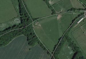 Property for sale by Auction Aerial view of a rural area with fields, trees, and a few roads. Pebble Lane and Crampshaw Lane intersect on the right side, near the outskirts of Ashtead. The landscape is predominantly green with scattered patches of woodland and agricultural fields. Buildings are sparse. Presented by World of Auctions