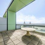 Property for sale by Auction A spacious rooftop terrace in a Liverpool penthouse investment apartment features a green and gray color scheme with a circular stone table at its center. The terrace offers a stunning view of the river and distant buildings under a clear blue sky. Presented by World of Auctions