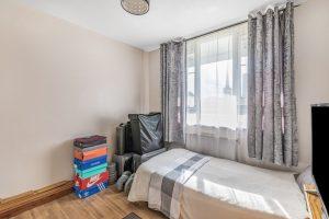 A small, tidy bedroom at Flat 3,1 Macclesfield House Central Street LONDON EC1V 8BA features light brown wood flooring and a single bed covered with a white and gray blanket. The window has sheer curtains and darker drapes. Stacks of colorful shoe boxes and a suitcase are placed beside the bed as sunlight filters through. This investment is for sale by auction. Presented by World of Auctions