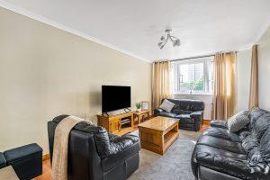 A cozy living room in Flat 3, Macclesfield House, Central Street LONDON EC1V 8BA features black leather sofas arranged around a wooden coffee table. A flatscreen TV sits on a wooden stand against the wall, with light-colored curtains framing a window that offers a view of nearby buildings. A small black stool is in the corner. Presented by World of Auctions