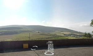 A scenic view of rolling green hills under a clear blue sky. In the foreground, part of a brick wall with a yellow waste bin can be seen. The road labeled "Channel Ave" runs along the bottom of the image. Land off Channel Avenue Porth Mid Glamorgan Wales (SOLD) by World of Auctions - other plots may be available; contact the auctioneers.
