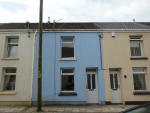 A row of three terraced houses at 73 Blaen CF48 3RB features a blue house in the middle, a pale yellow house on the left, and a beige house on the right. Each has distinct colored doors and window frames. A utility pole stands on the sidewalk in front of the blue house, offered on the market with World of Auctions.