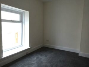 A small, empty room with beige walls and a dark carpet. There is a single window on the left side, letting in natural light. Located at 73 Blaen CF48 3RB, this property is on the market with World of Auctions.