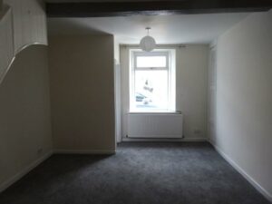 A small, empty room with white walls and a gray carpet. There's a single window in the center, a white radiator below it, and a white ceiling light. An alcove on the left and a closed door on the right complete this cozy space at 73 Blaen CF48 3RB, now on the market with World of Auctions.