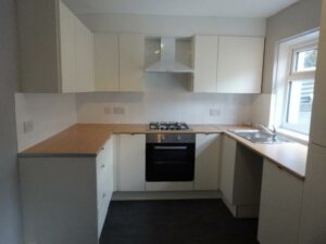 A modern kitchen with light-colored cabinets, a light wood countertop, and a dark floor. It features a built-in gas stove with an oven beneath, a range hood, a sink under a window, and ample counter space and storage. Now available at 73 Blaen CF48 3RB on the market with World of Auctions.