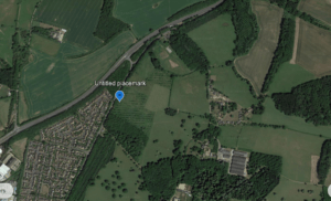 Aerial view of a plot of land at Home Farm, Hulcote, featuring green spaces, a suburban neighborhood, and a major roadway."