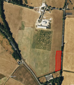Aerial view of farmland with a marked red rectangular plot on the right side. The plot is adjacent to a road labeled “Beech Farm Rd” and is surrounded by larger empty fields. Several buildings and structures are visible at the top center, with trees lining some field borders.