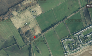 An aerial view shows a countryside landscape with fields, trees, and rural buildings. A red pin marks a specific location on a trail near a small group of trees. A residential area is visible along the bottom-right corner, hinting at the 24-acre leisure development site opportunity proposed for future development land at Anthorn. Nearby roads and pathways are also visible.