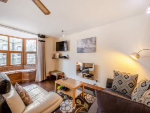 Property for sale by Auction A cozy living room at The Old Drapery Apartments, 12 Main St, Haltwhistle, features a mix of modern and rustic elements. It boasts a wall-mounted TV, a wooden coffee table, and comfortable sofas adorned with patterned cushions. A bay window with seating offers a bright view, and a floor lamp provides additional lighting. Now for sale by auction! Presented by World of Auctions