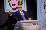 Property for sale by Auction An auctioneer, wearing a suit and tie, stands behind a lectern with "CHRISTIE'S" on it. He raises a hand, possibly making a bid announcement. In the background, there's a large image of Marilyn Monroe along with another indistinct artwork. Presented by World of Auctions