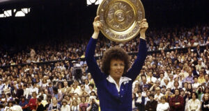 Property for sale by Auction A tennis player wearing a blue outfit with a white collar holds a large circular trophy above their head in front of a crowded stadium. The audience appears to be excited and engaged, with many people clapping and cheering. Presented by World of Auctions