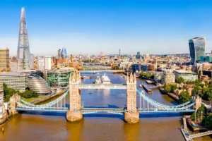 Property for sale by Auction Aerial view of London featuring the iconic Tower Bridge over the River Thames, with the Shard and other modern skyscrapers in the cityscape background under a clear blue sky. Presented by World of Auctions