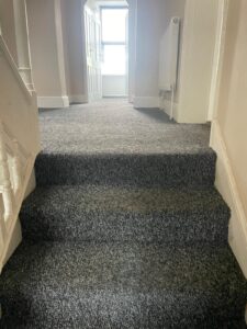 Property for sale by Auction A carpeted staircase and landing area in a house, leading to an open door with natural light shining through. The walls are painted in a light color, and a white radiator is mounted on the right wall. The floor beyond the doorway appears to be wooden. Presented by World of Auctions