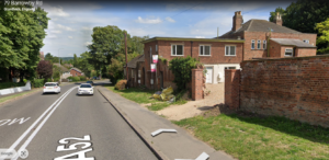 Property for sale by Auction A road with two cars on the left, bordered by trees and houses. A brick building with white garage doors is on the right side. The road has white double lines and is marked as A52. A sign reading "Barrowby Rd" is visible in the top left corner. Presented by World of Auctions