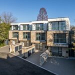 Property for sale by Auction A modern, multi-story apartment complex with a brick and glass exterior is now available as your new home for sale in Wimbledon. The building boasts large windows and balconies, surrounded by trees and a paved driveway under a clear blue sky. Presented by World of Auctions