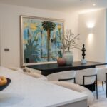 Property for sale by Auction A modern dining area in a Wimbledon new home for sale features a black table, white chairs, and decorative vases. An abstract painting with palm trees graces the wall. A marble countertop holds a bowl of apples, while large glass doors open to an inviting outdoor space. Presented by World of Auctions