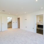 Property for sale by Auction Spacious empty room with white walls and beige carpet in this Wimbledon new home for sale. An open door reveals a staircase, while recessed lighting fixtures adorn the ceiling. A sliding door leads to a bathroom featuring a modern sink and dark tile flooring, all in a minimalist design. Presented by World of Auctions