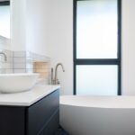 Property for sale by Auction This Wimbledon new home for sale boasts a modern bathroom with a minimalist design, featuring a white vessel sink on a dark vanity, an inviting large bathtub, and a frosted window that complements the light gray subway-tiled walls. Presented by World of Auctions