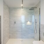 Property for sale by Auction A modern bathroom in this Wimbledon new home for sale features a large walk-in shower with white subway tiles, a glass partition, a rainfall showerhead, and a handheld shower. The room also includes a chrome towel radiator and a sleek, wall-mounted toilet. Presented by World of Auctions
