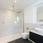 Property for sale by Auction Discover a modern bathroom in this Wimbledon new home for sale, featuring a glass-enclosed shower, white subway tile walls, and a rain showerhead. Highlights include the floating toilet and vanity with a white vessel sink, complemented by a large mirror and stainless steel towel warmer on dark tile floors. Presented by World of Auctions
