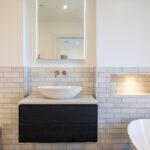 Property for sale by Auction Discover a Wimbledon new home for sale featuring a modern bathroom with white subway tiles, a wall-mounted faucet, and a round vessel sink on a dark cabinet. Enjoy the elegance of a freestanding bathtub, mirrored cabinet above the sink, and thoughtfully lit recessed shelving. Presented by World of Auctions