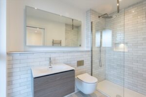 Property for sale by Auction Discover a modern bathroom in this Wimbledon new home for sale. It boasts white subway tile walls, a glass-enclosed shower, a wall-mounted toilet, and a wooden vanity with sink. A large mirror sits above the vanity, enhanced by well-placed ceiling lights for optimal illumination. Presented by World of Auctions