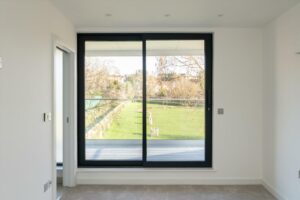 Property for sale by Auction A bright room in this Wimbledon new home for sale features large sliding glass doors opening to a balcony with views of a grassy lawn and trees. The minimalist interior, with light-colored walls and carpeting, creates an airy atmosphere. Presented by World of Auctions