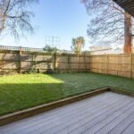 Property for sale by Auction A backyard with a wooden deck and grassy lawn bordered by a wooden fence gleams under the clear, sunny sky, perfect for hosting Wimbledon watch parties. A few bare trees and a small palm tree add charm to this inviting new home for sale. Presented by World of Auctions