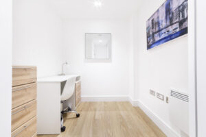 Property for sale by Auction Minimalist room with a white desk and chair, wooden drawers, and a modern painting on the wall. The space has light wood flooring and a square mirror above the desk, creating a clean and bright atmosphere. Presented by World of Auctions