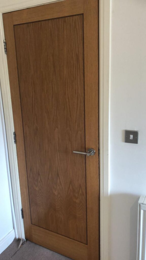 Property for sale by Auction A closed wooden door with a silver handle is shown against a white wall. To the right of the door, a light switch is mounted on the wall. The floor is carpeted in a neutral color. Presented by World of Auctions