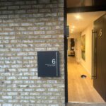 Property for sale by Auction A brick building with a partially open door marked "6" invites curiosity. A sign reads "Orchard Grove, Wimbledon," hinting at charm within. New home for sale, the interior boasts wood flooring with a pair of shoes near the entrance. Presented by World of Auctions