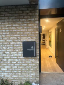 Property for sale by Auction A brick building with a partially open door marked "6" invites curiosity. A sign reads "Orchard Grove, Wimbledon," hinting at charm within. New home for sale, the interior boasts wood flooring with a pair of shoes near the entrance. Presented by World of Auctions