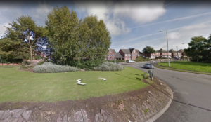 Property for sale by Auction A roundabout with green grass and a few trees in the center is surrounded by residential houses, including a block of investment apartments for sale. Road signs are placed at the edge of the roundabout, all set under a partly cloudy sky in Newcastle Stoke on Trent. Presented by World of Auctions