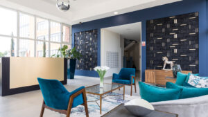 Property for sale by Auction Modern lounge with blue and gray tones featuring velvet chairs, a glass coffee table, and a gold-accented reception desk. Decorative wall panels and a potted plant add to the elegant decor. Presented by World of Auctions