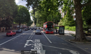 Property for sale by Auction A street view of Maida Vale in London, showcasing two red double-decker buses by a bus stop, with several cars on the road. Tall trees line the street, and buildings stand in the background. This vibrant area offers a unique hotel redevelopment opportunity amidst its classic charm. Presented by World of Auctions