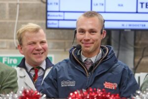 Property for sale by Auction Two men stand in front of a screen. The man on the right wears a headset and a jacket with logos. They both smile, with festive red decorations in the foreground. Presented by World of Auctions