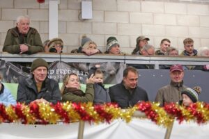 Property for sale by Auction A group of people, including adults and children, are gathered on a balcony overlooking an event. They are dressed warmly in coats and hats. The balcony is decorated with red and gold garland. Some people are leaning on the railing, watching intently. Presented by World of Auctions