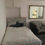 Property for sale by Auction Nestled within an investment apartment in Brighton BN3, this small bedroom features a bed with white sheets and pillows against the wall. A large mirror on the adjacent wall reflects both space and style, while a beige couch peeks out, adding charm to this auction-listed gem. Presented by World of Auctions