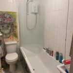 Property for sale by Auction This investment apartment in Brighton BN3, available for sale by auction, features a well-appointed bathroom with a white bathtub and shower, neatly arranged toiletries, and a striking painting of a person with a headdress resting near the toilet against pristine white tiled walls. Presented by World of Auctions
