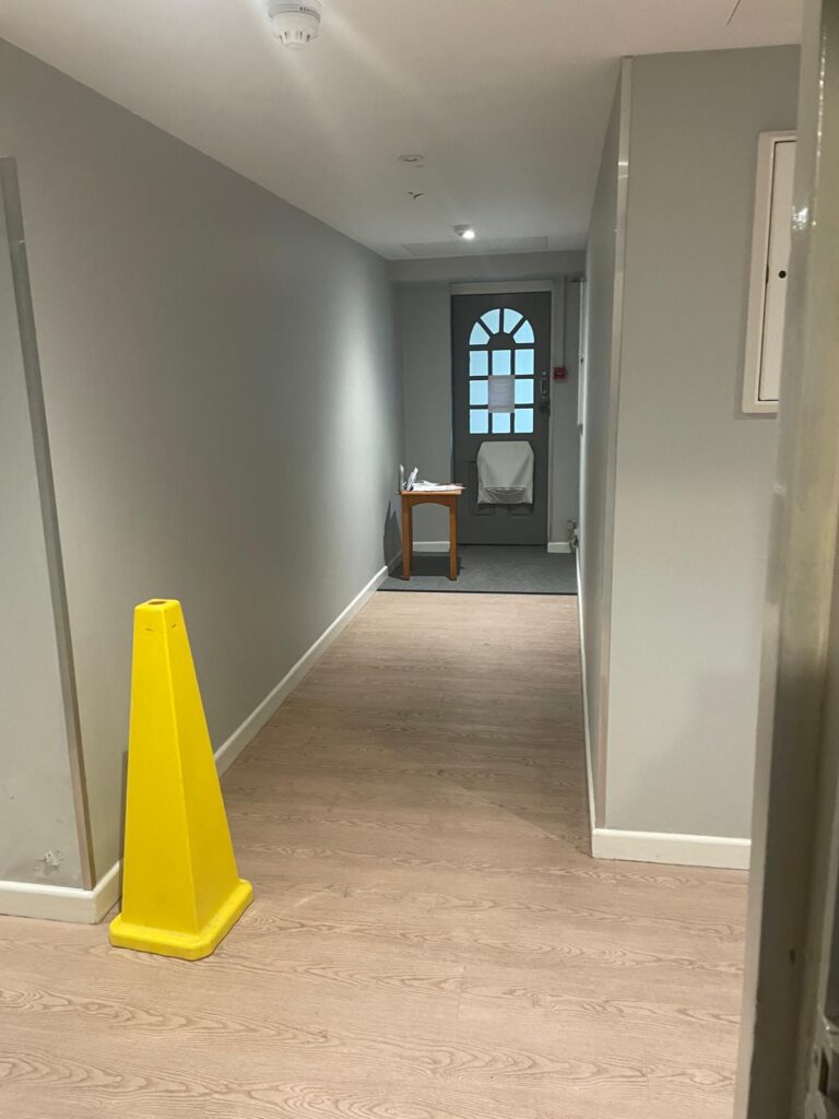 Property for sale by Auction A hallway with light wooden flooring and gray walls leads to a door with an arched window in this investment apartment for sale by auction. A small table with a chair sits near the door, while a yellow caution cone is placed nearby, adding charm to the Brighton BN3 property. Presented by World of Auctions
