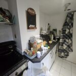 Property for sale by Auction The cluttered kitchen counter in this charming investment apartment in Brighton BN3 for sale by auction features various food items, containers, and appliances. A Coca-Cola mirror hangs above, while a checkered cloth is draped on the right. The white floor contrasts with dark countertops. Presented by World of Auctions
