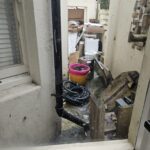 Property for sale by Auction A cluttered outdoor area, visible through a window, hints at potential in this investment apartment in Brighton BN3 for sale by auction. With items like buckets, hoses, and a washing machine scattered about, the space appears narrow and messy, featuring a drainpipe and window on the left. Presented by World of Auctions