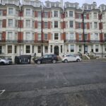 Property for sale by Auction A row of five-story red brick buildings with white accents and ornate railings stands proudly in Brighton BN3. Three cars are parked on the street in front, alongside trash bins. With a cloudy sky overhead, this investment apartment is for sale by auction. Presented by World of Auctions