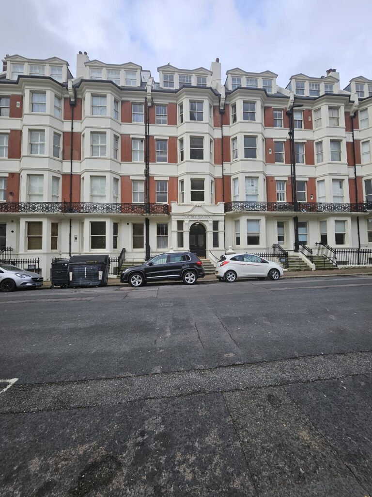 Property for sale by Auction A row of five-story red brick buildings with white accents and ornate railings stands proudly in Brighton BN3. Three cars are parked on the street in front, alongside trash bins. With a cloudy sky overhead, this investment apartment is for sale by auction. Presented by World of Auctions